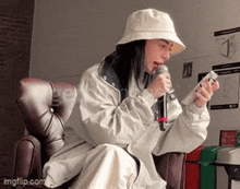 a woman wearing a hat is singing into a microphone while holding a cell phone