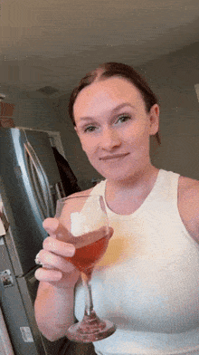 a woman in a white tank top holds a wine glass