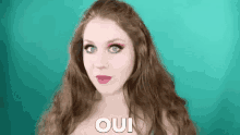 a woman with long red hair and pink lipstick is making a funny face and saying oui .