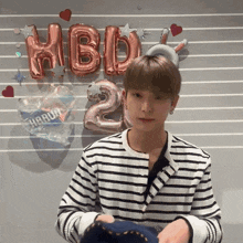 a man in a striped shirt is standing in front of balloons that say hbd 2