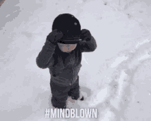 a baby is standing in the snow wearing a hat .
