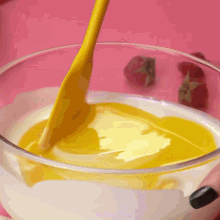 a yellow spoon is pouring yellow liquid into a bowl