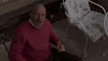 a bald man in a red sweater and glasses is sitting at a table with his mouth open .