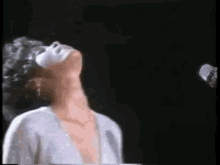 a woman is singing into a microphone on a stage while wearing a white dress .