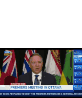 a man in a suit and tie is giving a speech in front of a row of flags