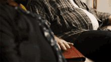 a man in a plaid shirt is sitting on a couch with his hands on his lap .