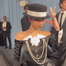 a woman wearing a black hat and pearls is making a funny face