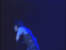 a man in a vest is dancing on a stage with his arms outstretched in the dark .