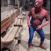 a man in a spider man costume stands in front of a bench