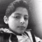a black and white photo of a young boy sitting in a chair .