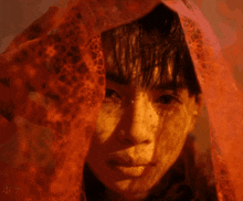 a close up of a person 's face with a red lace covering their face