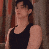 a man in a black tank top leaning against a wall with his eyes closed
