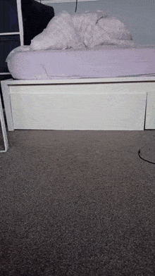 a white bed with a purple comforter is sitting on a grey carpet