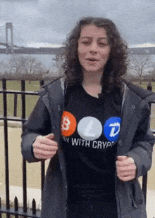 a woman wearing a shirt that says " play with crypto " is standing in front of a bridge