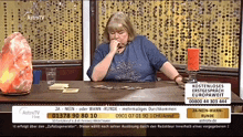a woman sits at a table in front of a screen that says astrotv