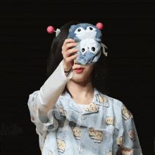 a woman wearing a pajama top holds a stuffed animal over her face