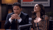 a man and a woman are sitting in front of a dimera enterprise sign