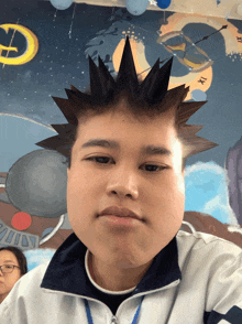 a boy with a spiky mohawk looks at the camera in front of a mural that says xii