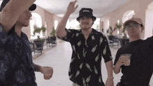 three men are standing next to each other in a hallway . one of the men is wearing a hat .
