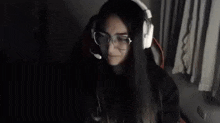 a woman wearing headphones and glasses is sitting at a desk in a dark room .