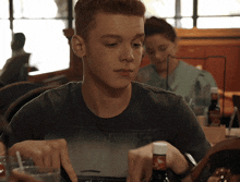 a young man is sitting at a table with a bottle of beer