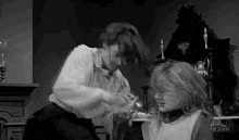 a black and white photo of a woman cutting another woman 's hair in a room .