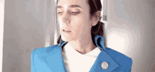 a woman is wearing a blue jacket and a white shirt with a button on the collar .