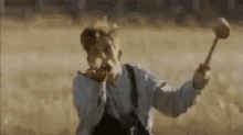 a man with a beard is holding a hammer in a field and making a funny face .