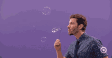 a man in a polka dot shirt and tie is blowing soap bubbles against a purple background .