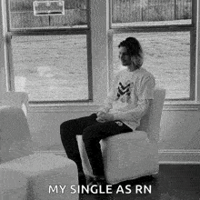 a man is sitting in a chair in front of a window and says `` my single as rn '' .