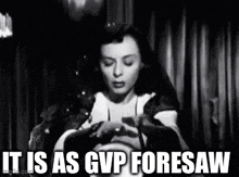 a black and white photo of a woman sitting in front of a curtain .