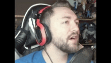 a man with a beard is wearing headphones and talking into a microphone while sitting in a chair .