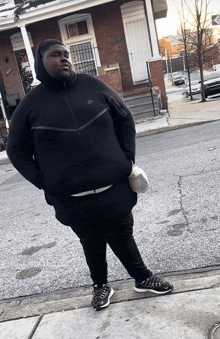 a man wearing a black nike hoodie is standing on the sidewalk