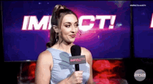a woman is holding a microphone in front of a tv screen that says impact .