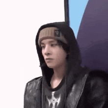 a young man wearing a hooded jacket and a beanie is sitting in a chair .