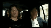 a man in a suit is driving a car with a young boy in the back seat .
