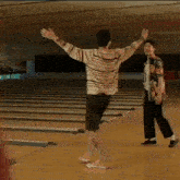 a man in a striped shirt is carrying another man on his shoulders in a bowling alley