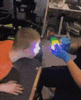 a person wearing blue gloves is holding a rainbow light in front of a child 's face