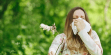 a woman is blowing dandelion seeds into her nose while holding a dandelion .
