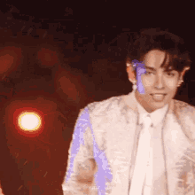 a young man in a white suit and tie is standing on a stage in front of a red light .
