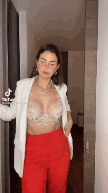 a woman wearing a white jacket and red pants is standing in a hallway .