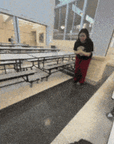 a girl in a black shirt and red pants stands in front of a row of tables