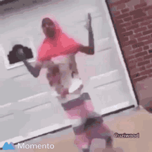 a woman in a pink hijab is standing in front of a garage door holding a baby .