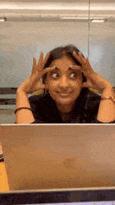 a woman is sitting in front of a laptop computer with her hands on her face .
