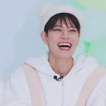 a young man wearing a white hat and a white hoodie is laughing and smiling .