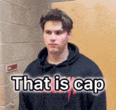 a man wearing a black hoodie is standing in front of a door that says that is cap