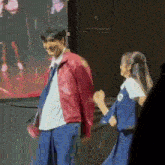 a man in a red jacket is standing next to a woman in a blue dress .