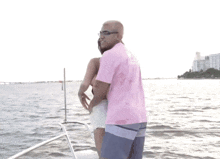 a man in a pink shirt stands next to a woman in shorts on a boat