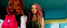 a woman with pink hair and a red backpack is standing next to another woman with red hair .