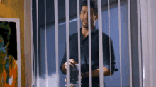 a man in a blue shirt is holding a glass in front of a window